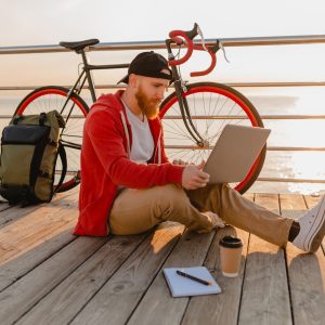 handsome hipster style bearded man working online freelancer on laptop with backpack and bicycle in morning sunrise by the sea healthy active lifestyle traveler backpacker handsome hipster style bearded man working online freelancer on laptop with backpack and bicycle in morning sunrise by the sea healthy active lifestyle traveler backpacker